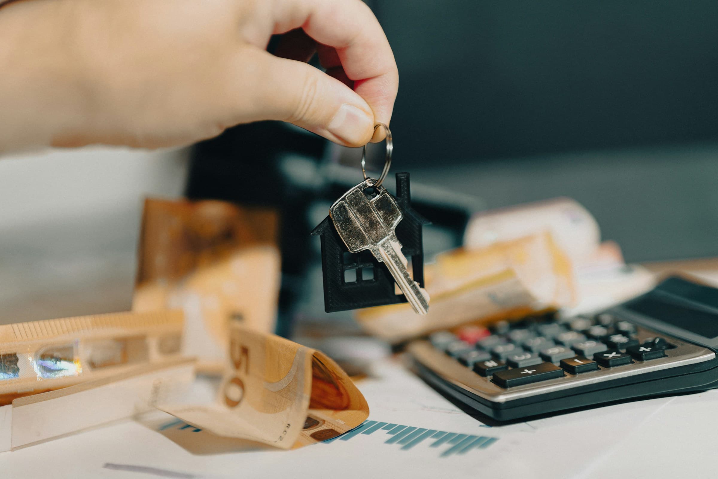 Hand holding house keys in front of a calculator and real estate finance documents