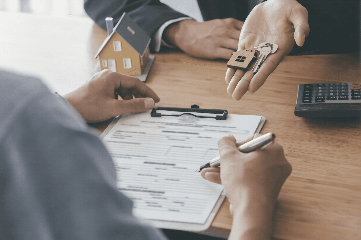 Buyer reviewing a real estate document while keys and a model house are handed over across a desk